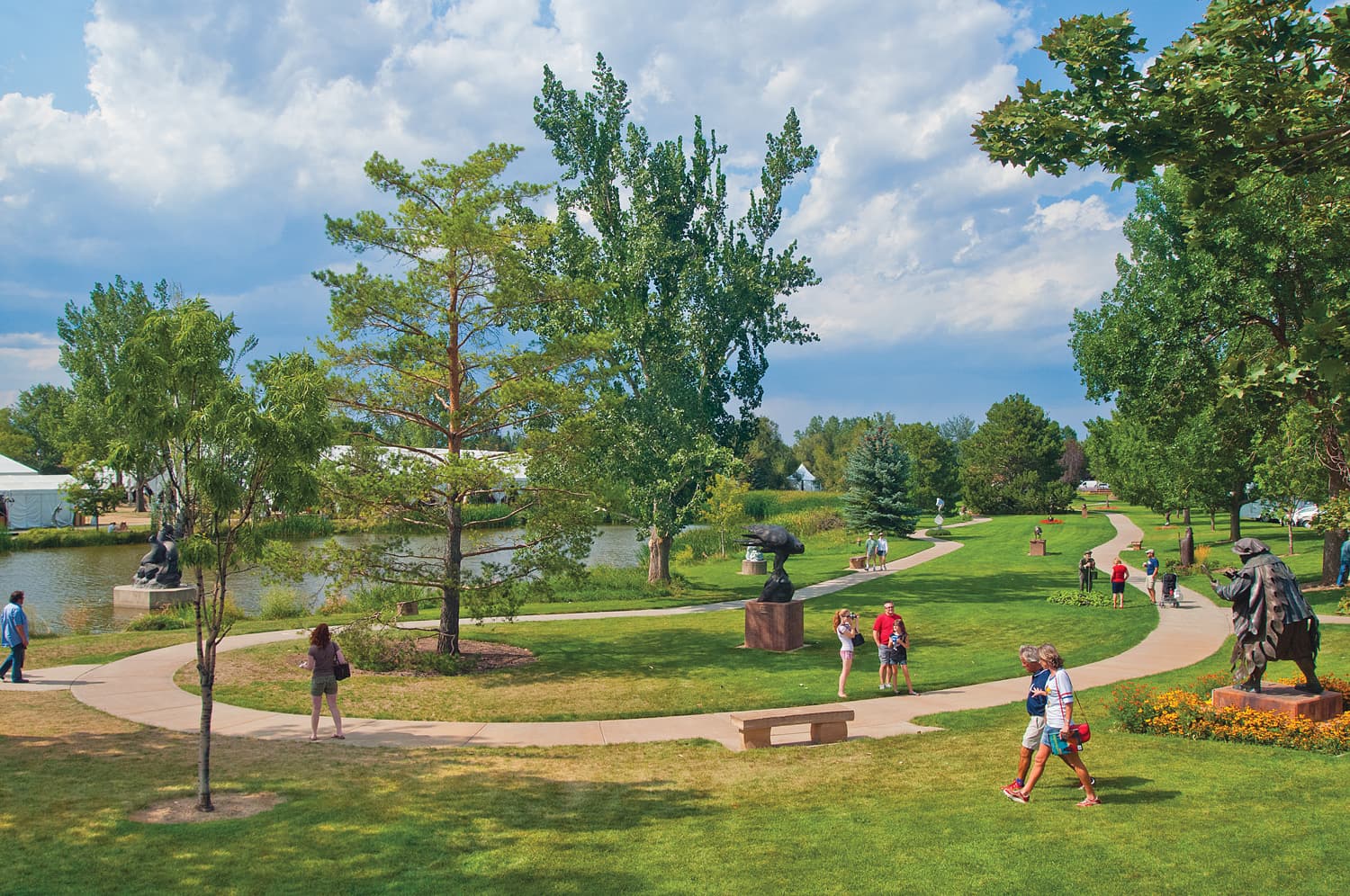 People walk on a path surrounded by green grass and sculptures at Benson Sculpture Garden in Loveland