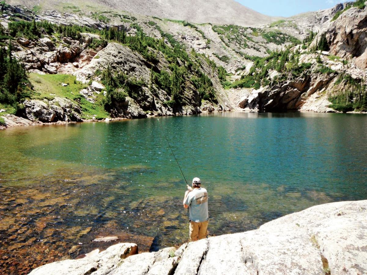 A person fly-fishing on a sparkling lake with Kirks Flyshop