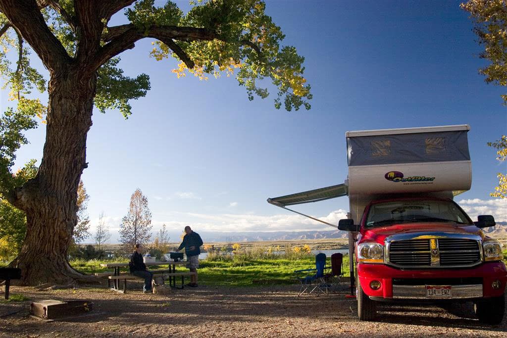 Next to a gigantic tree, a pickup truck with a fold-out awning sets up camp as dusk settles in