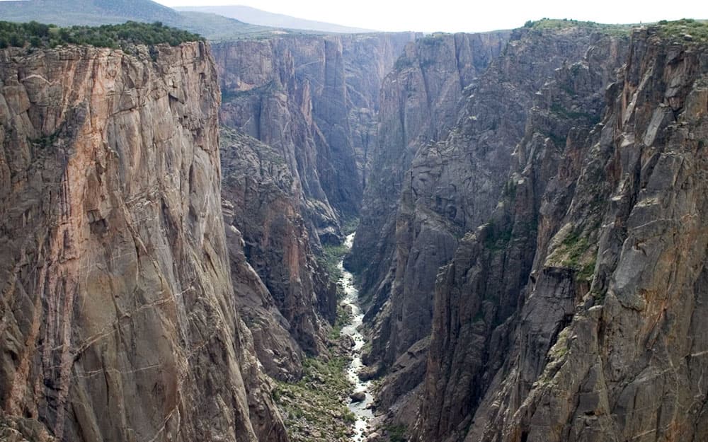 At the bottom of the deep Black Canyon of the Gunnison National Park, a rushing river pushes its way along the valley floor.