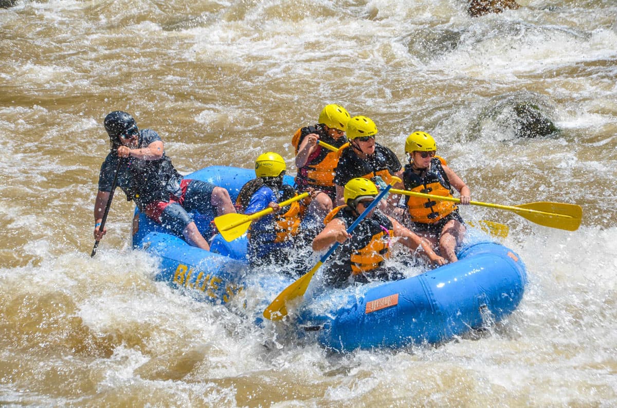 A group of people paddle through whitewater river rapids in a blue raft near Aspen, Colorado.