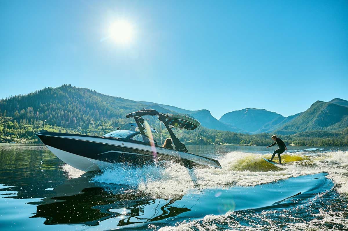 A water skier hits big waves on the lake with mountains rising behind him