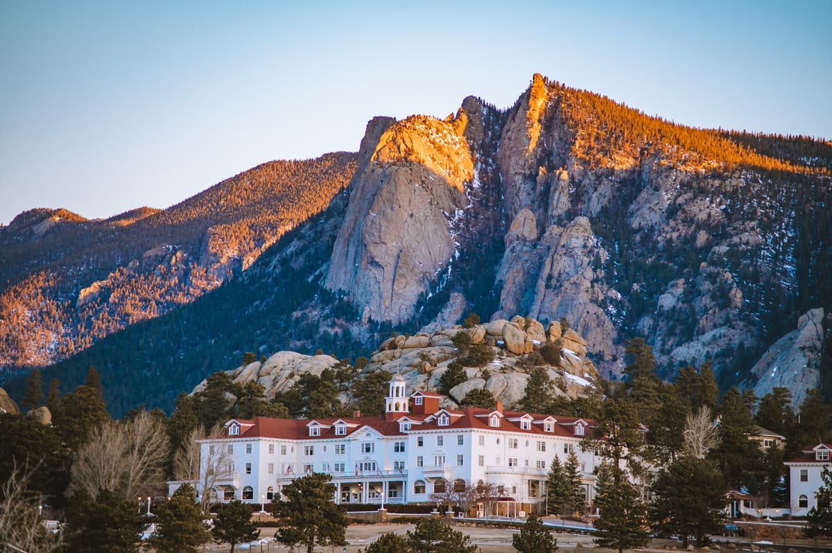 The Stanley Hotel in Estes Park, Colorado — a beautiful white historical hotel with a red roof and mountains rising in the background.