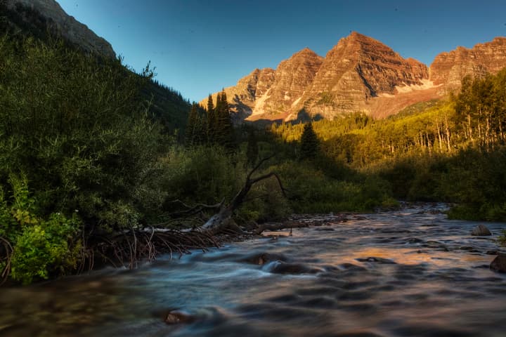 The sun shines on two mountain peaks, while in their shadow, a river runs through it