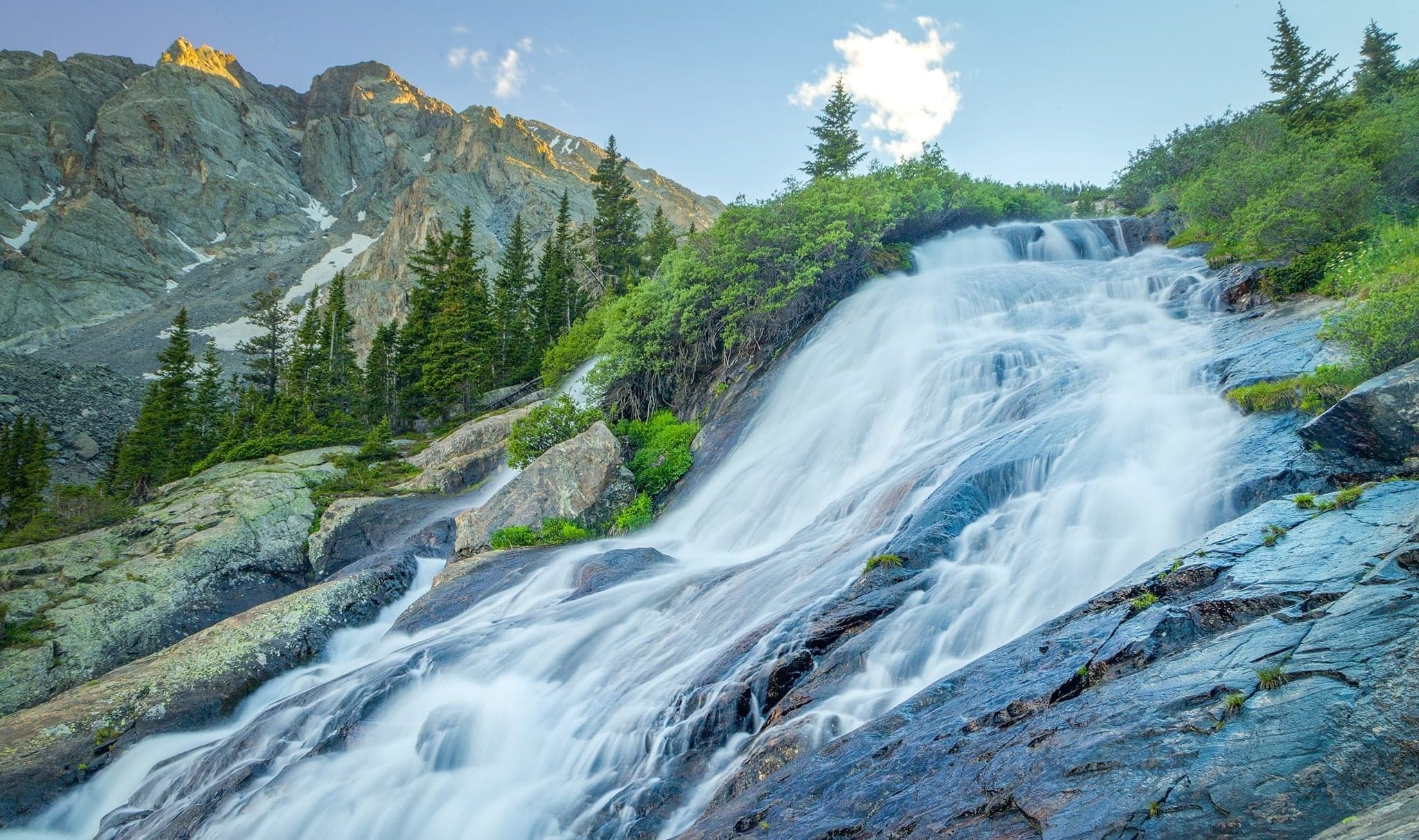 Blue water pours through McCullough Gulch Falls in Breckenridge surrounded by greenery