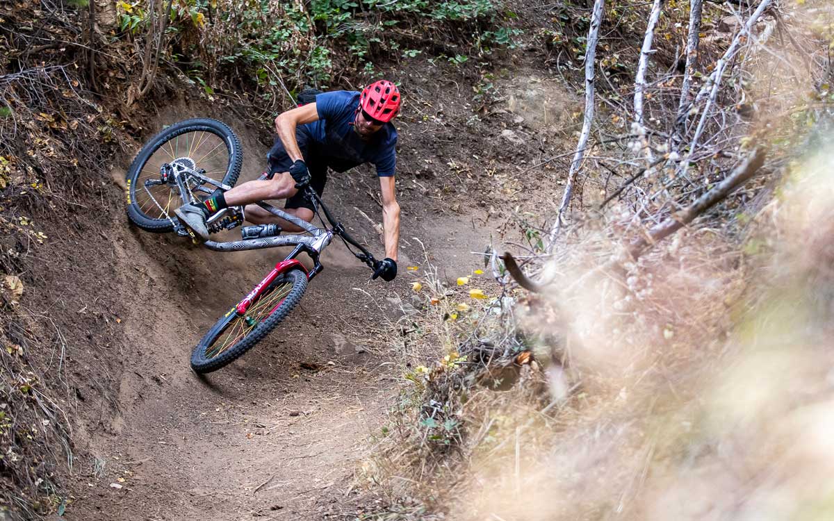 A mountain biker wearing a red helmet drifts on a bike down a steep dirt track of a mountain in Colorado.