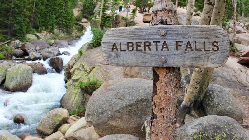 A sign reads Alberta Falls with water rushing in the background in Rocky Mountain National Park