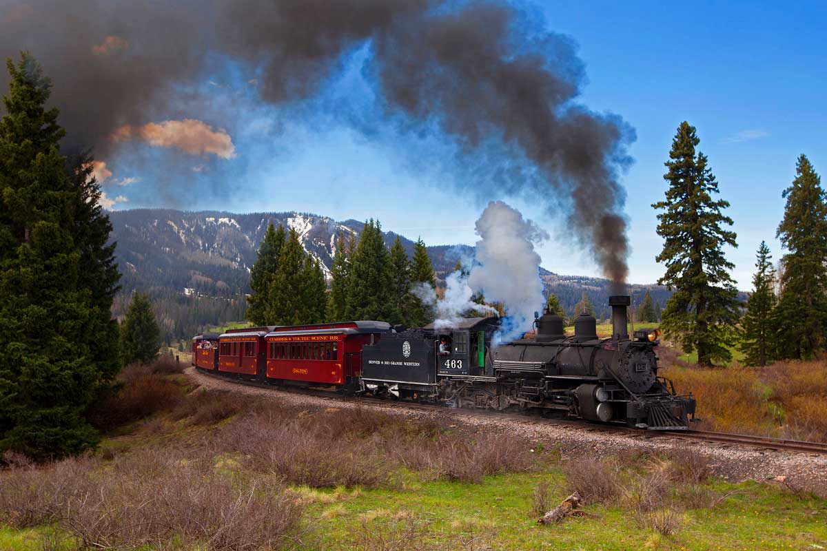 A locomotive rolls through a scenic mountain landscape