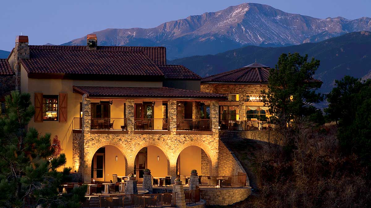 A brick, castle-like building is lit from below and a mountain peak rises behind it