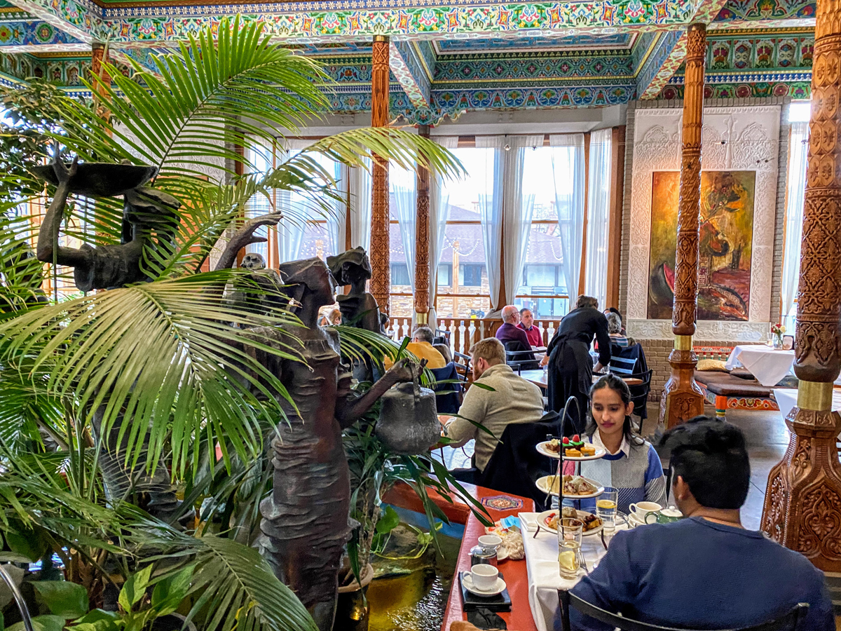 An interior shot of people dining at Boulder Dushanbe Teahouse surrounded by tropical plants, pillars with ornate carving and colorful mosaiced tiles