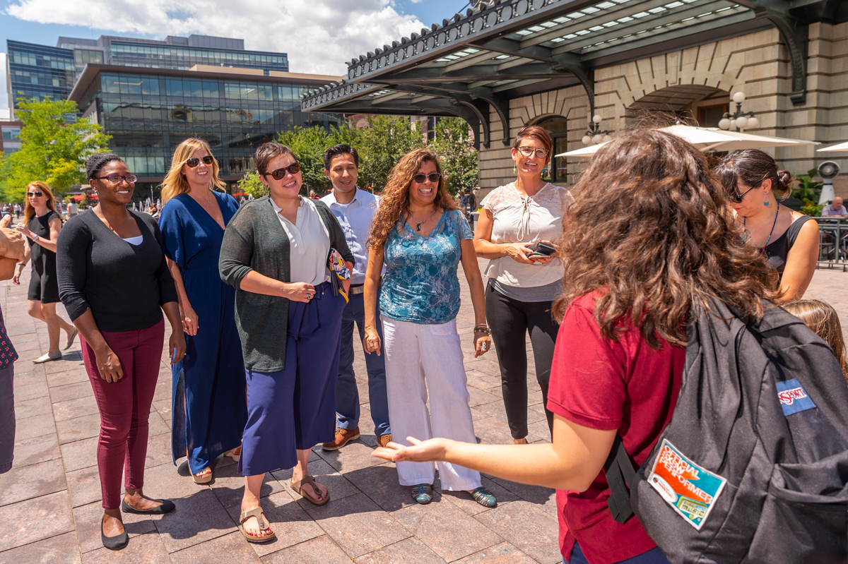 A group of visitors listens to a guide during a historic walking tour in downtown Denver near Union Station.