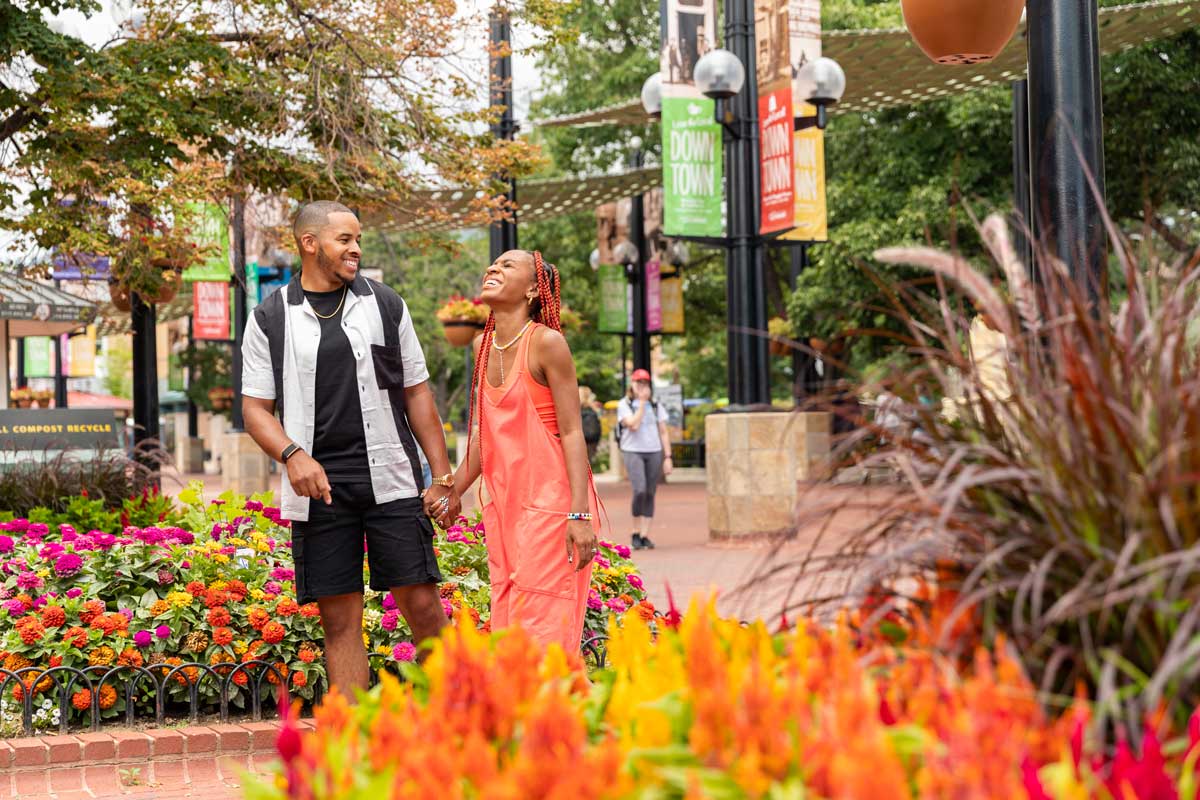 A couple laughs and has a good time while strolling Pearl Street Mall in Boulder, Colorado among pots of bright summer flowers.