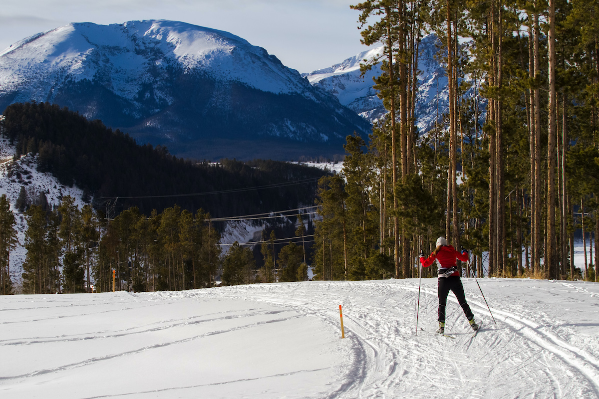 In a vast, flat, snowy meadow, a cross-country skier in a red jacket pushes foward using their poles