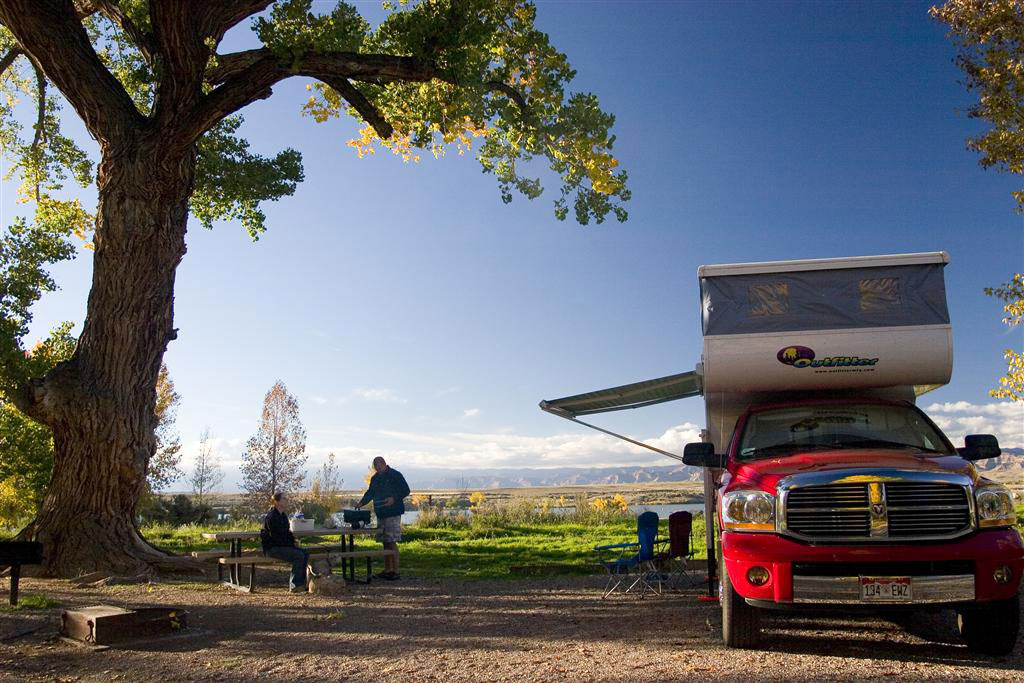Next to a gigantic tree, a pickup truck with a fold-out awning sets up camp as dusk settles in