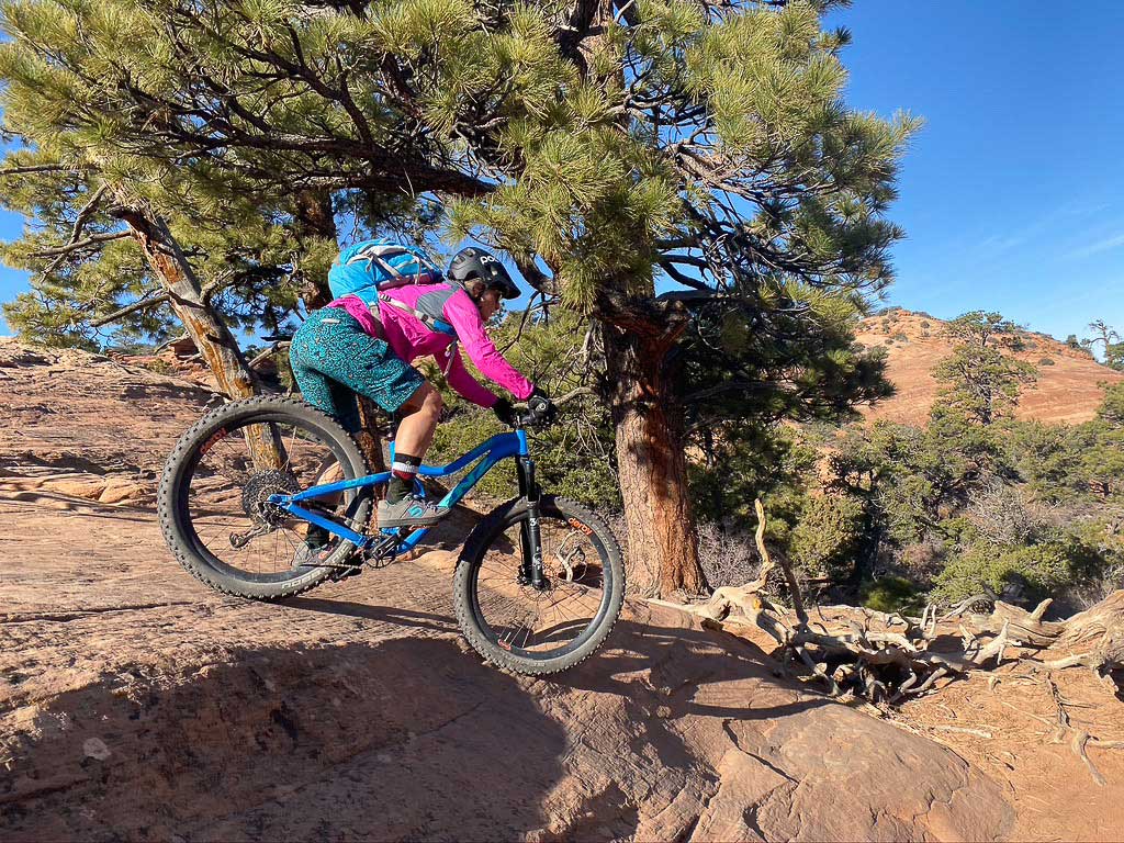 A cyclist in bright pink and blue clothes rides an electric-blue mountain bike down a rocky descent in Colorado.
