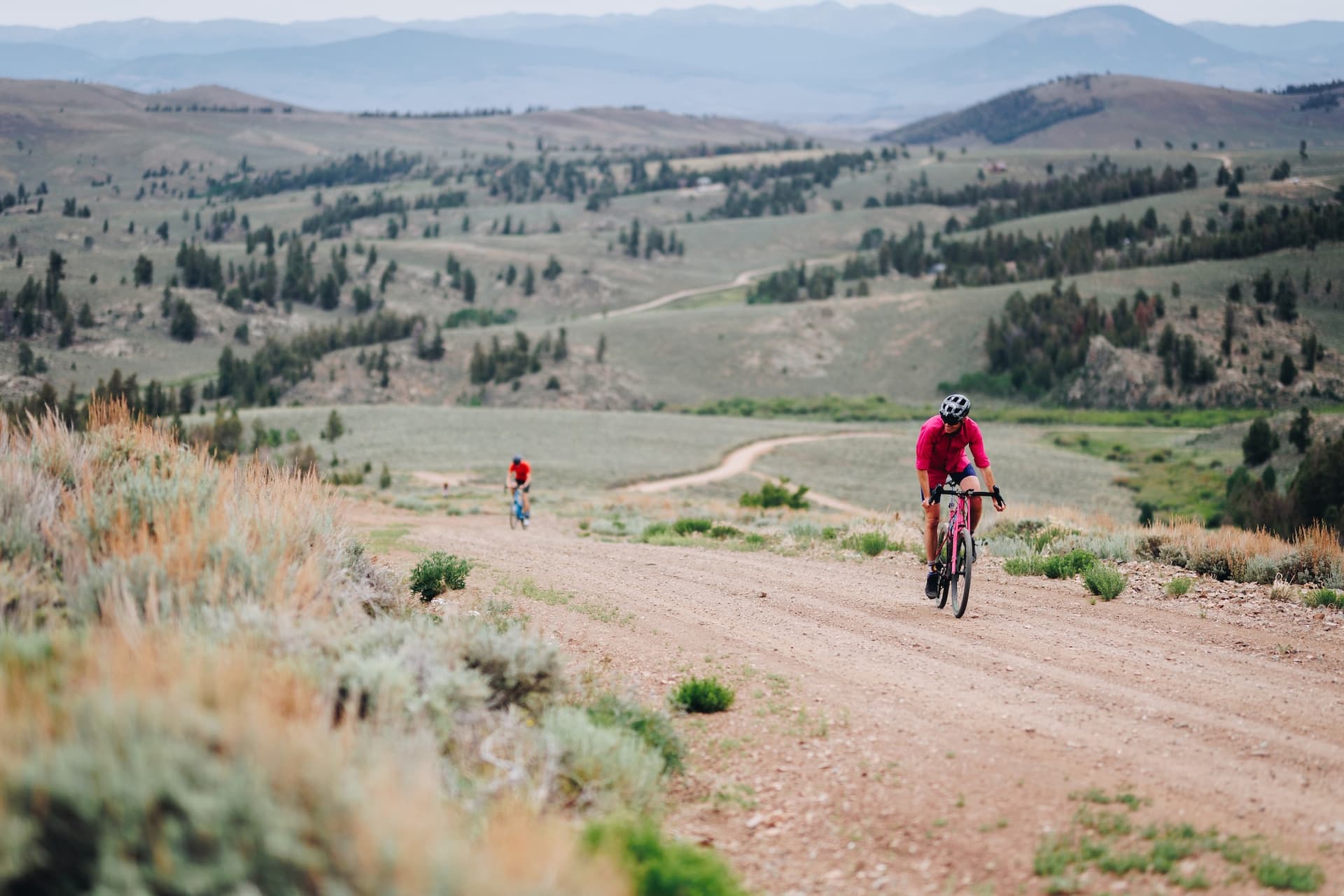 Cyclists riding on a gravel road along a winding path with rolling hills in the background in Gunnison and Crested Butte, Colorado.