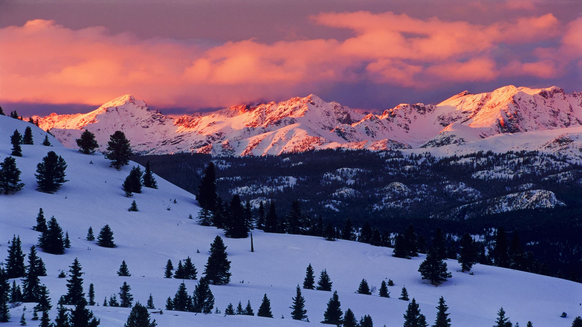 the alpenglow during the Vail Colorado sunset tints the sky pink over snowcapped mountains