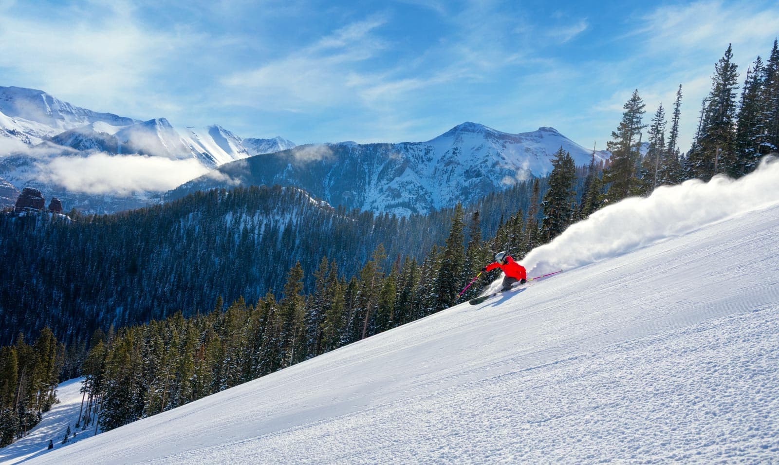 A skier blows up some powder as they charge downhill under sunny Colorado skies