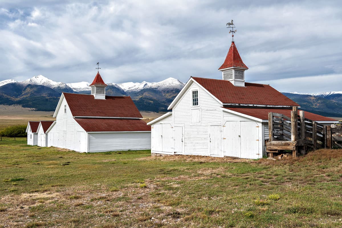 White barn buildings with red roofs with mountain backdrop in Westcliffe, Colorado.