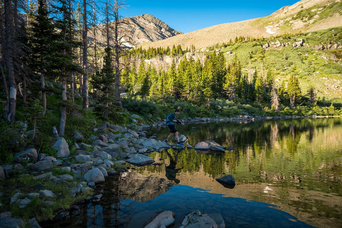 Hiker stepping on rocks with reflecting lake below in Westcliffe, Colorado.