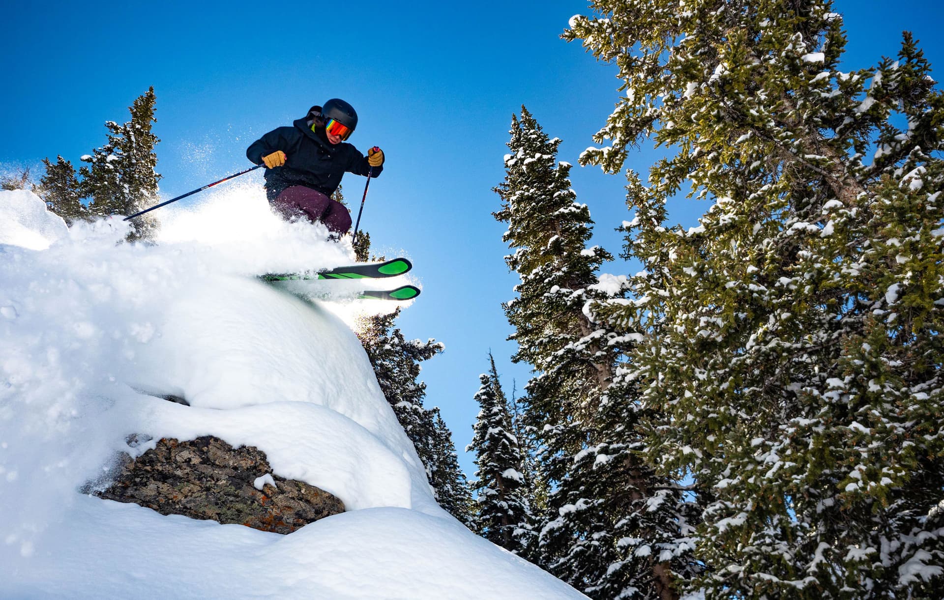 A skier about to make a jump going downhill with tall pines in the background in Gunnison and Crested Butte, Colorado.