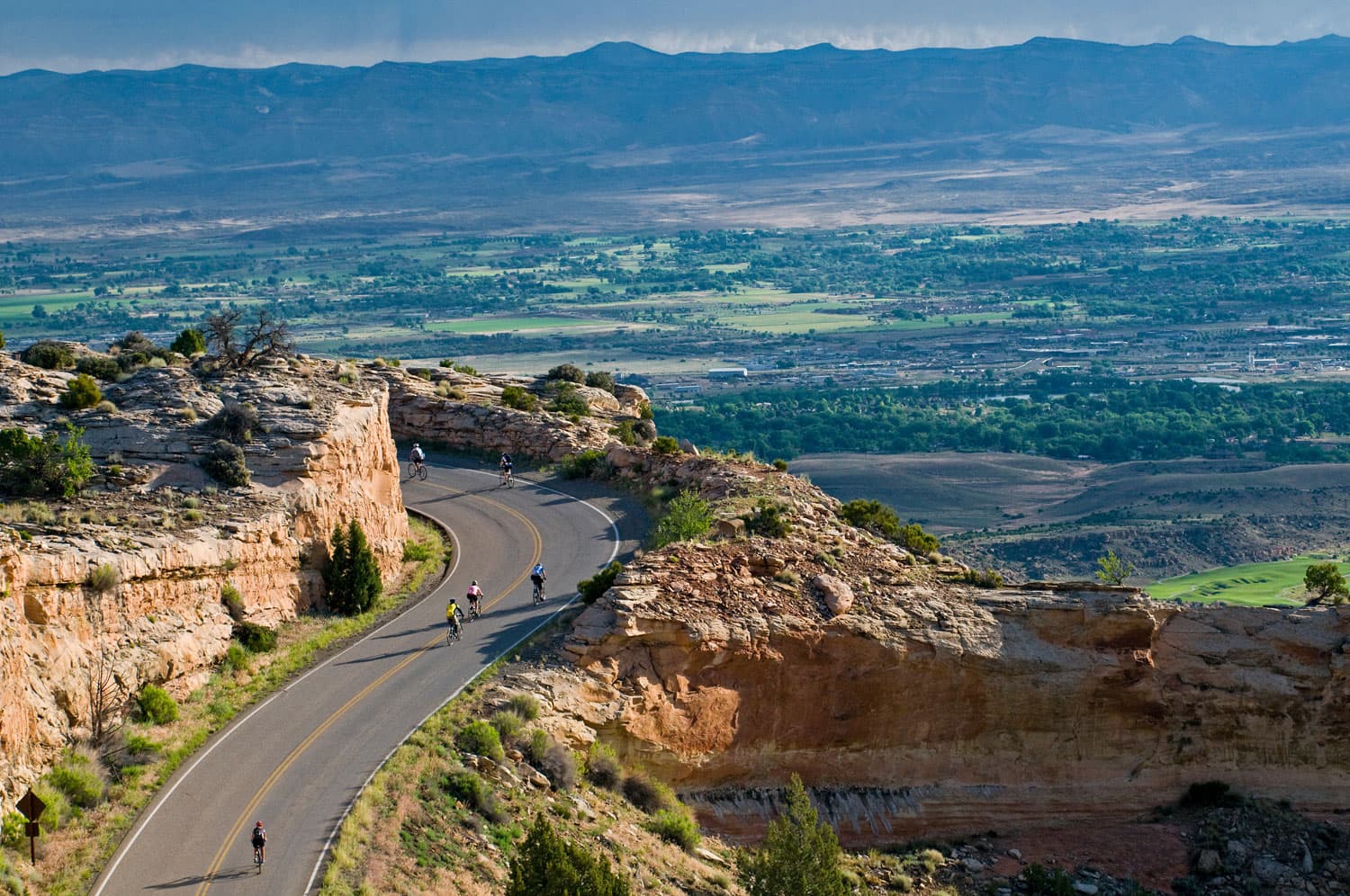 Bikers ride along a mountain road with a beautiful valley spread out below