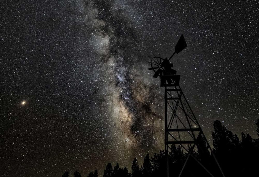 An old-school windmill with a view of the Milky Way and the night sky's stars.