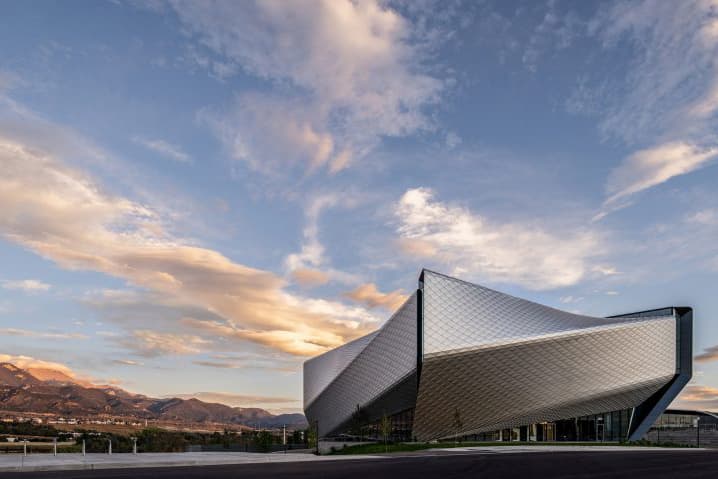 A silver building that resembles and folded origami boat stands alone in Colorado. White, paved paths allow visitors to enter and walk around.
