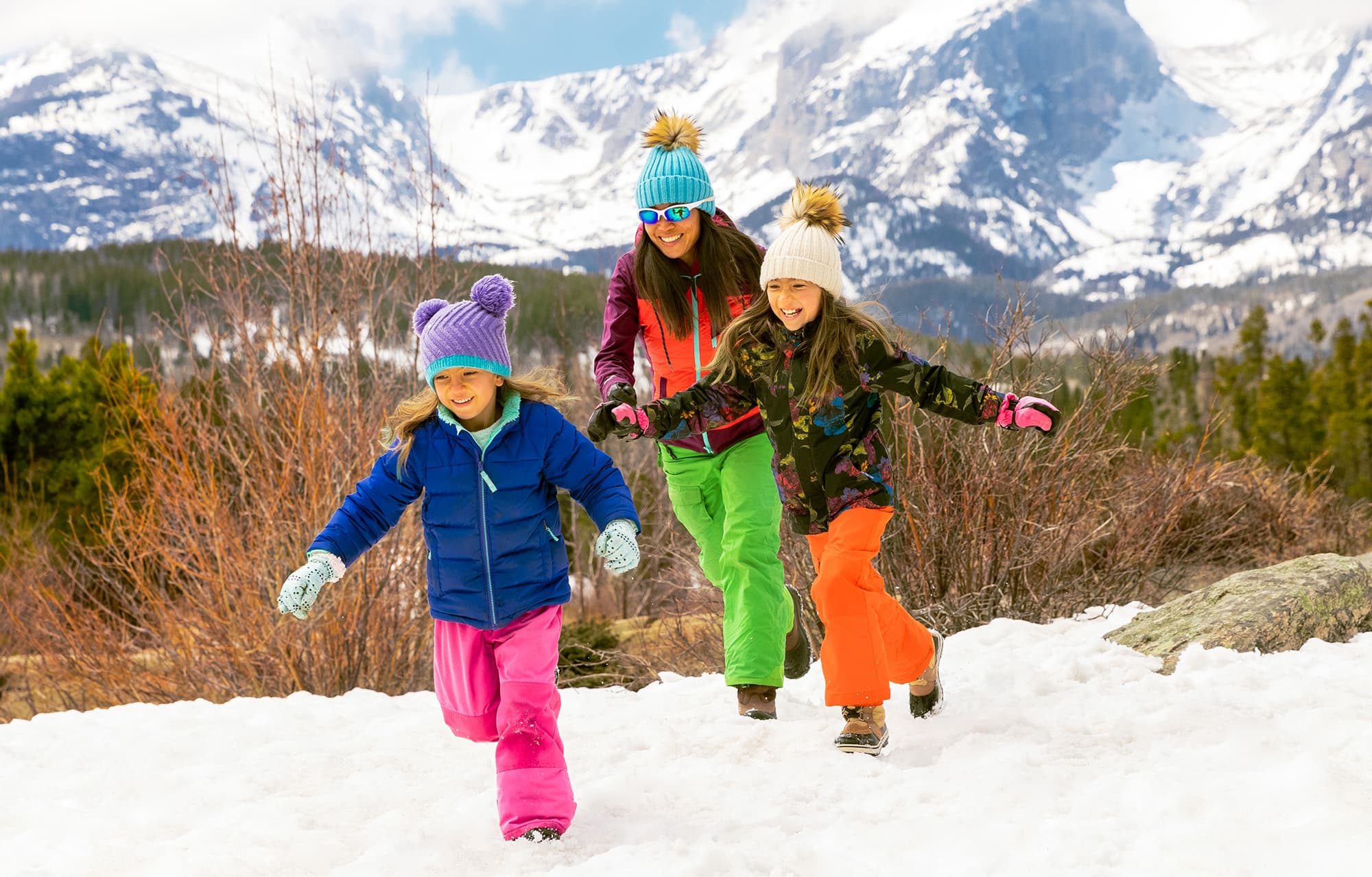 A family playing in the snow at Rocky Mountain National Park with snowy mountains in the background