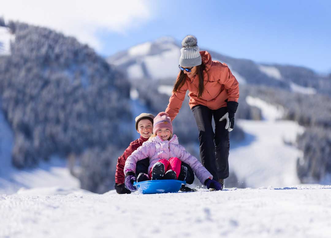 A woman pushes two children on a sled