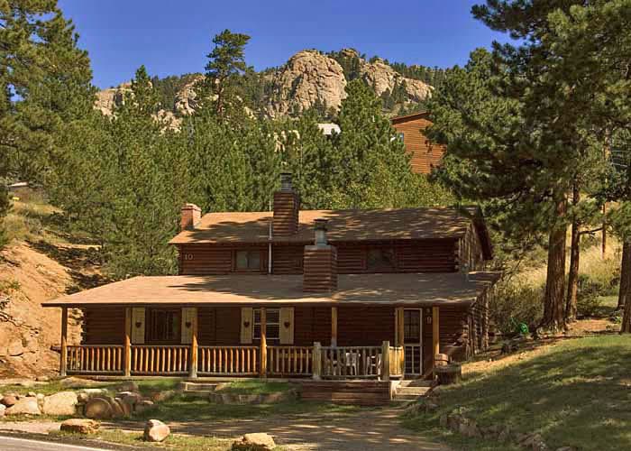 Black Hawk Lodge's log cabin surrounded by green trees and mountains outside Rocky Mountain National Park, Estes Park, CO