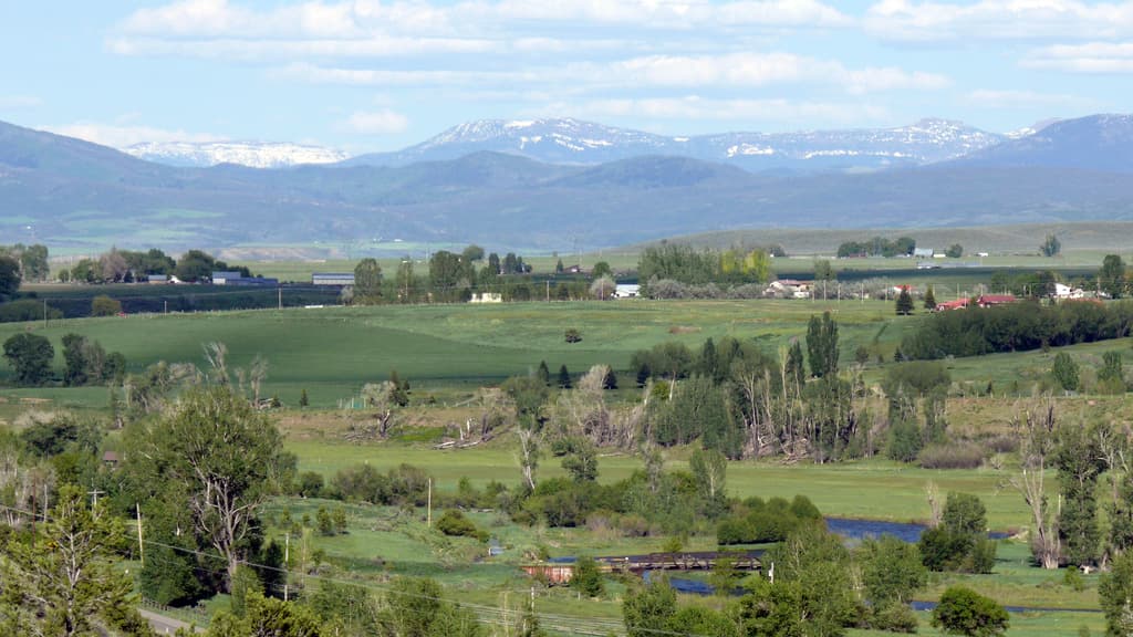 A view of the green White River Valley with snowcapped mountains sitting under puffy white clouds in the distance.