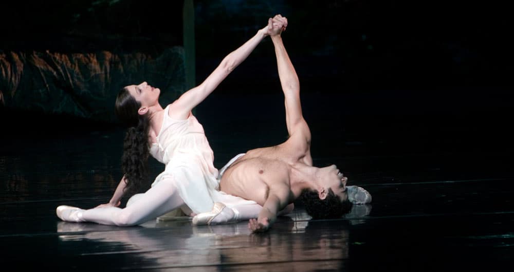 Two ballet dancers are paused in a dramatic pose on the floor of a stage with their hands clasped at the Vail International Dance Festival in Vail, Colorado.