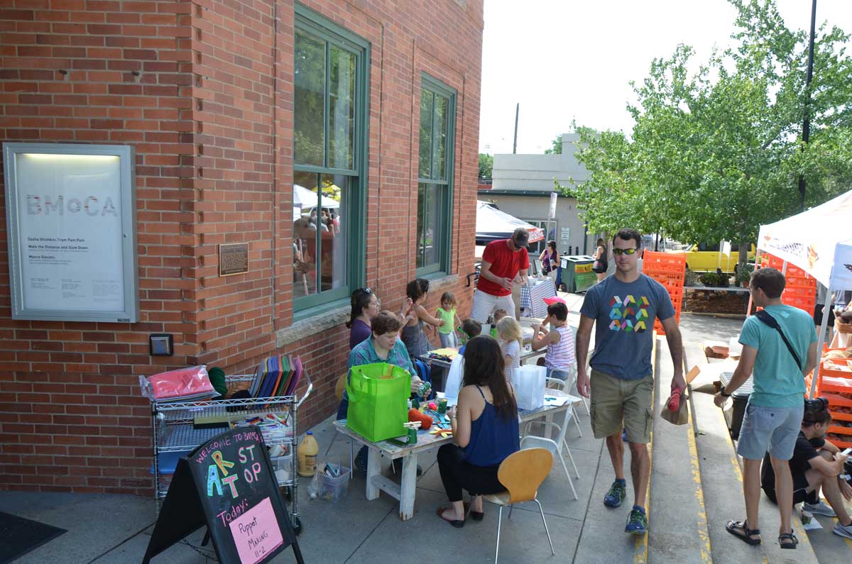 At BMoCA Art Stop, kids and adults sit at tables in front of the museum doing various crafts.