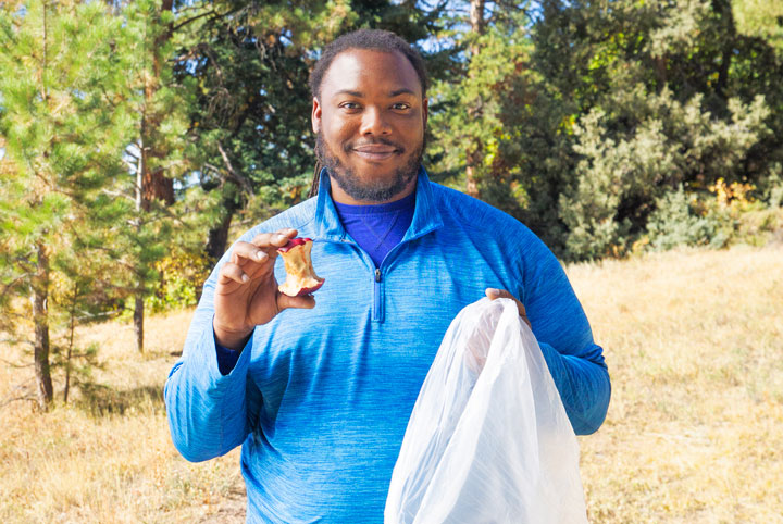 Hiking content creator, Nelson Holland holds an apple core and a trash bag. He is demonstrating that you need to throw away your eaten apple instead of throwing it on the ground while hiking