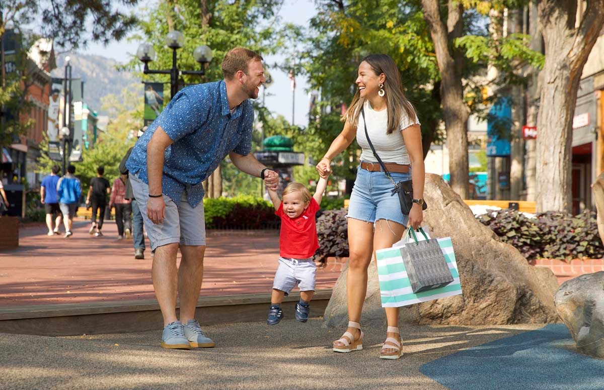 Two adults swing a child between them as they walk along the pedestrian mall