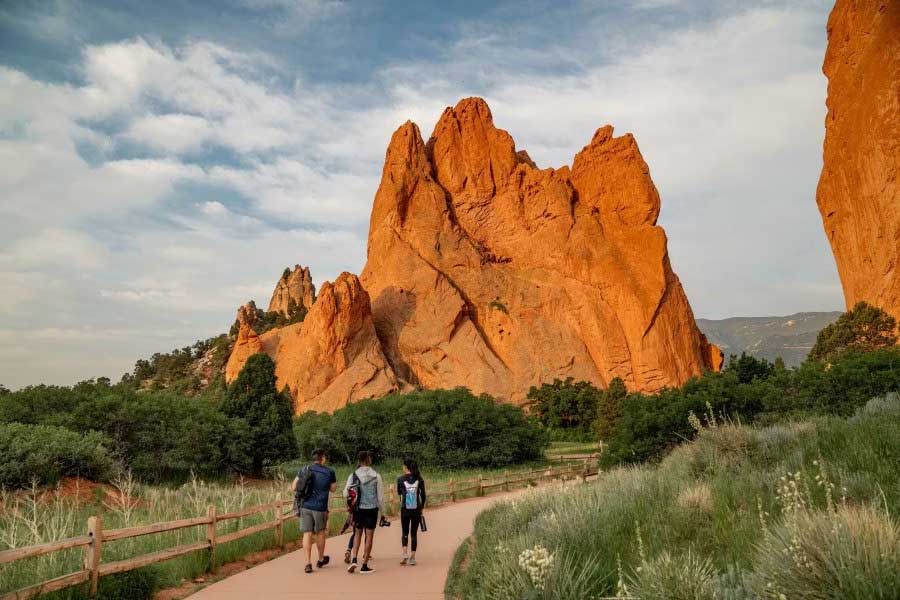Three people walk a paved trail between giant rock formations