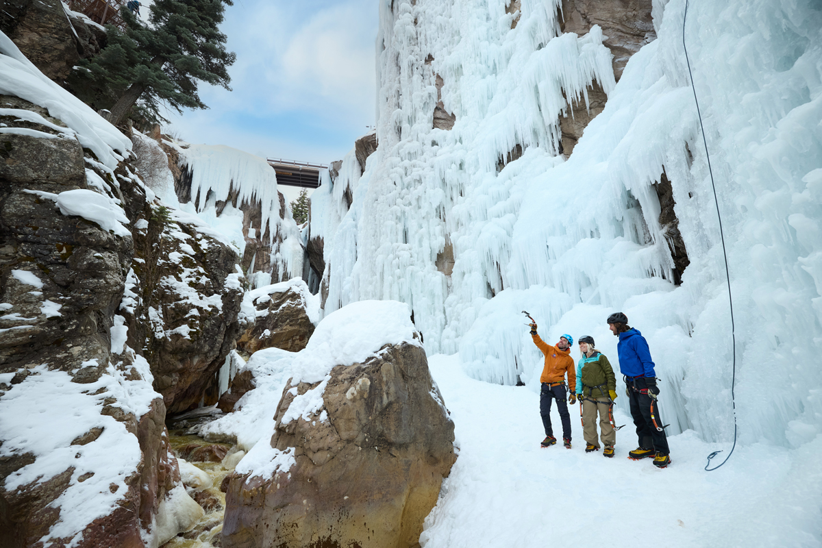 A group of people stand in the bottom of an icy and snowy canyon preparing to climb a sheet of ice at Ouray Ice Park in Colorado