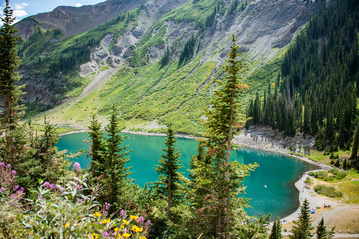 An aerial view of Emerald Lake's shocking green alpine waters with tall evergreens in the foreground.