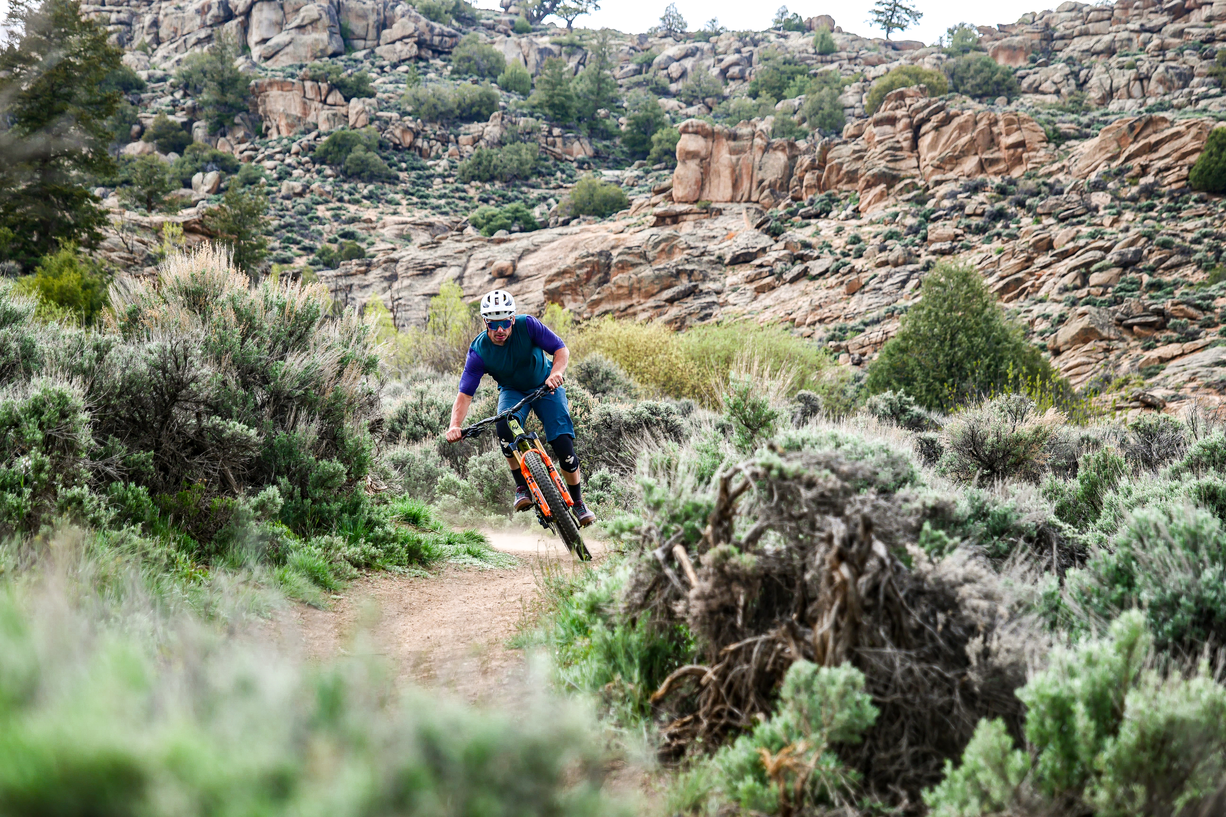 A mountain biker rides a dirt trail through green landscapes with a backdroup of rocks at Hartman Rocks in Gunnison, Colorado.