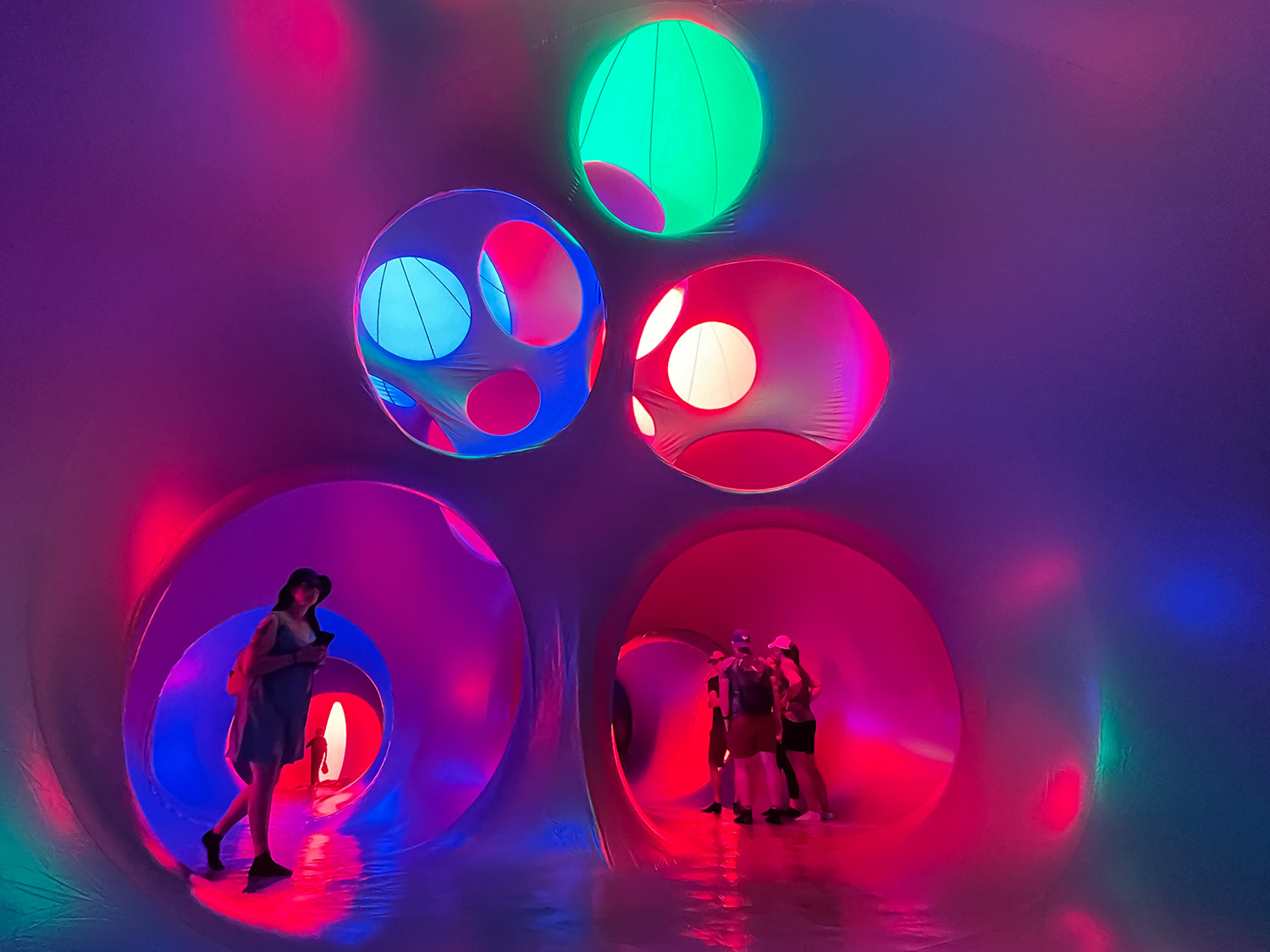 People crawl through colorful purple tunnels amid lights of blue, green and red at Aurora Borealis Festival in Aurora Colorado