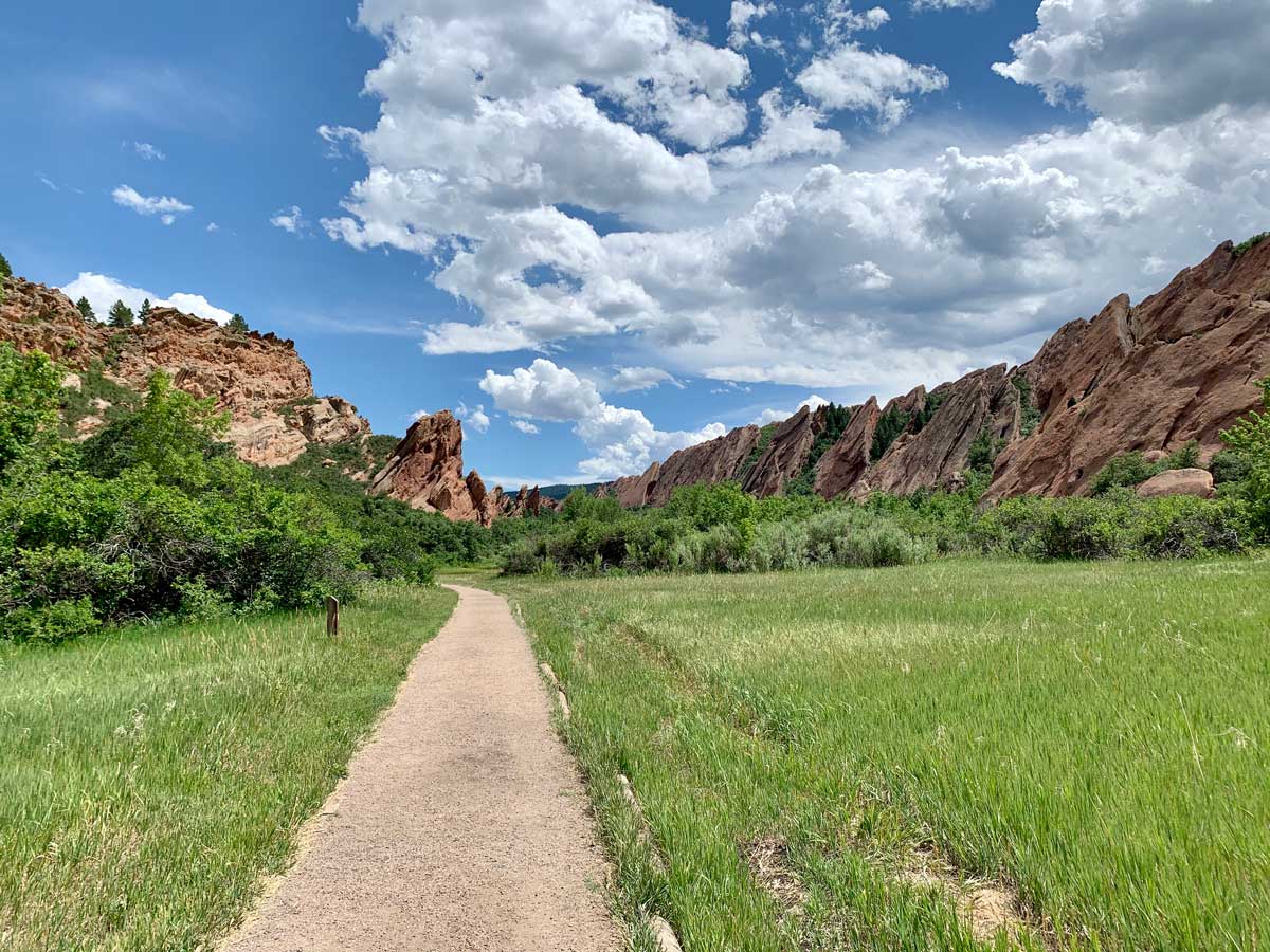A dirt trail leads through a grassy meadow to red-rock formations in Roxborough State Park