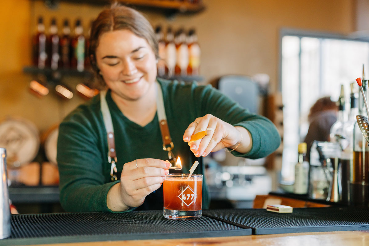 Bartender igniting a cocktail garnish with a flame at 477 Distilling in Greeley, Colorado.