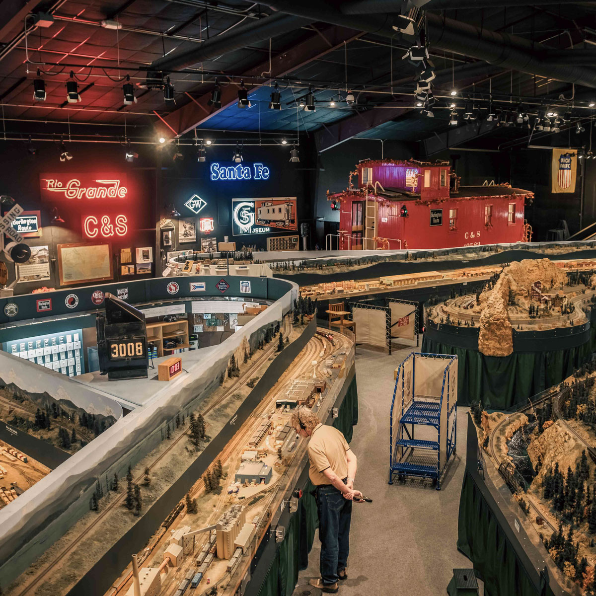 Aerial view inside the Colorado Model Railroad Museum showing miniature trains and a visitor.