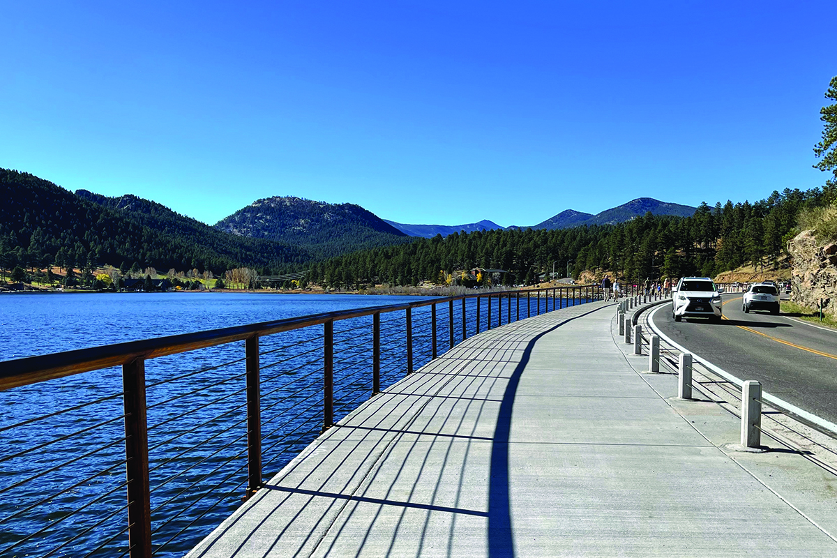 Evergreen Lake Trail with road on the right and the lake on the left, distant mountains in background.
