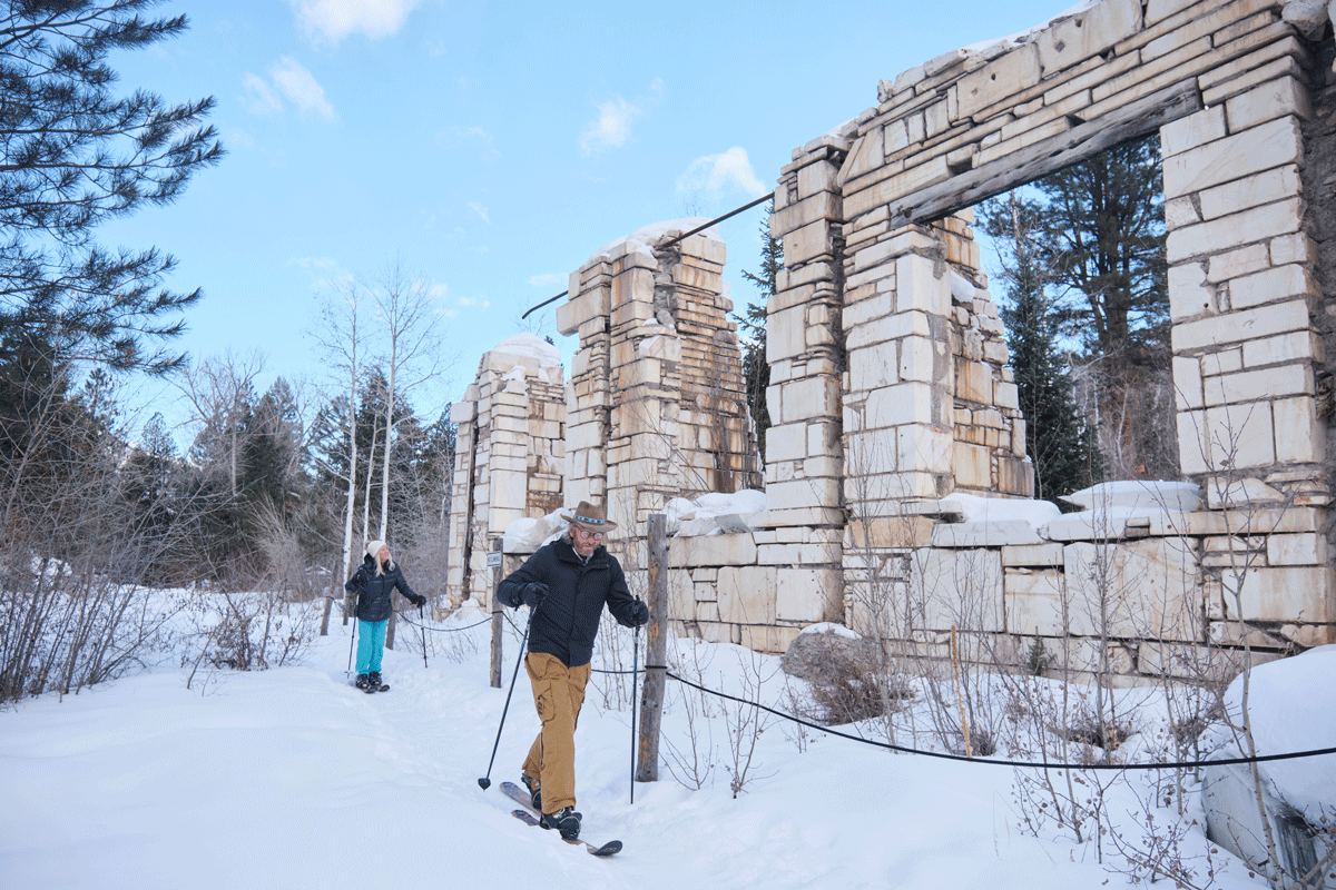 Family skiing on flat ground past a rocky wall in Marble, Colorado.
