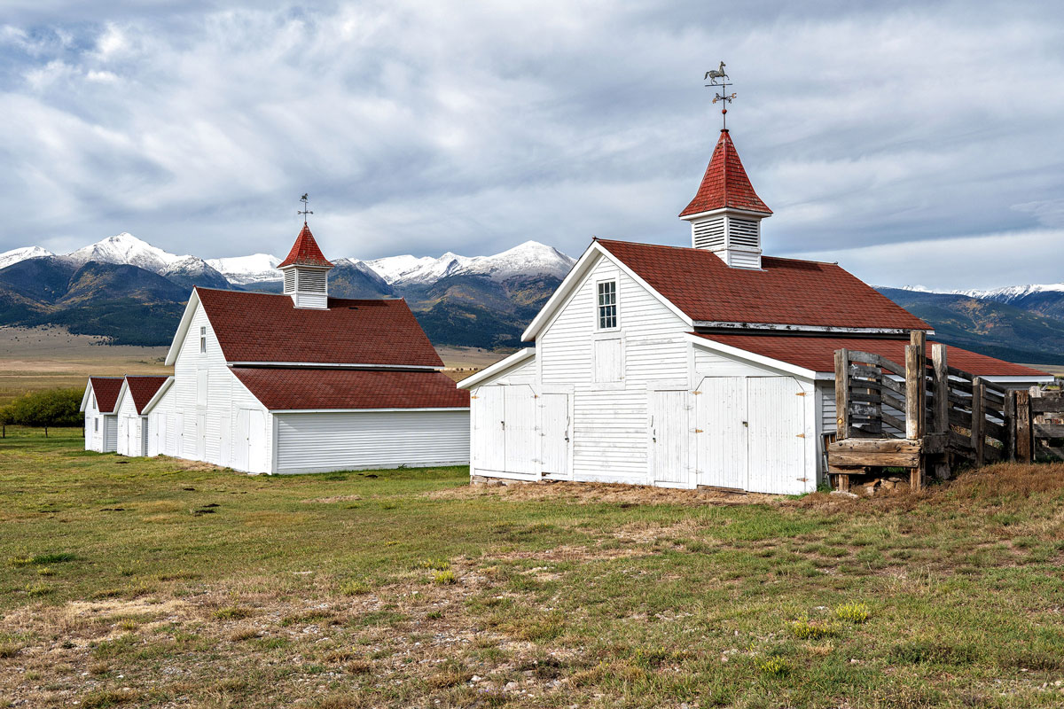 White barn buildings with red roofs with mountain backdrop in Westcliffe, Colorado.