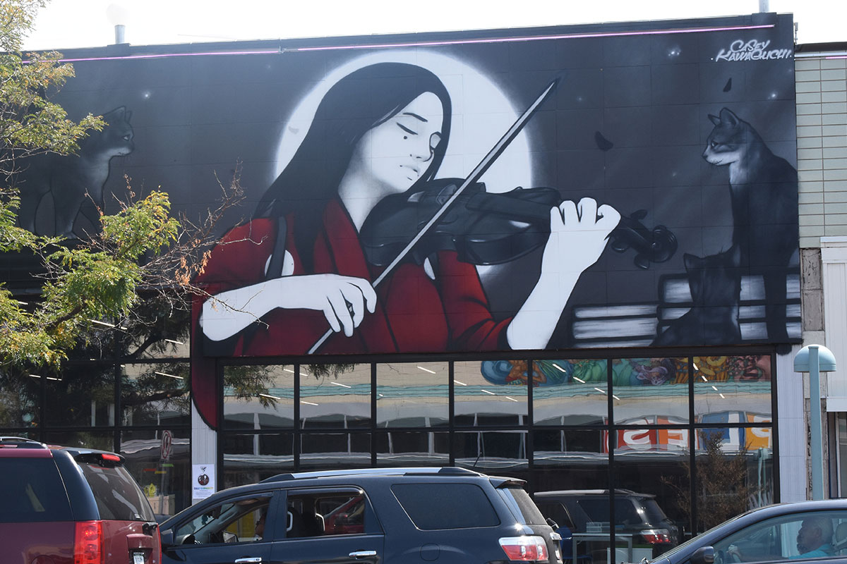 A mural of a woman playing the violin painted on the side of a building in Aurora, Colorado