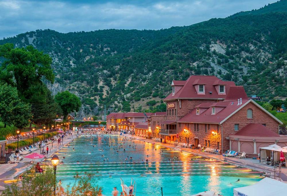 Post lamps and lights on the resort building keep massive, rectangular hot springs pool lit for guests to use in the evening in Colorado.