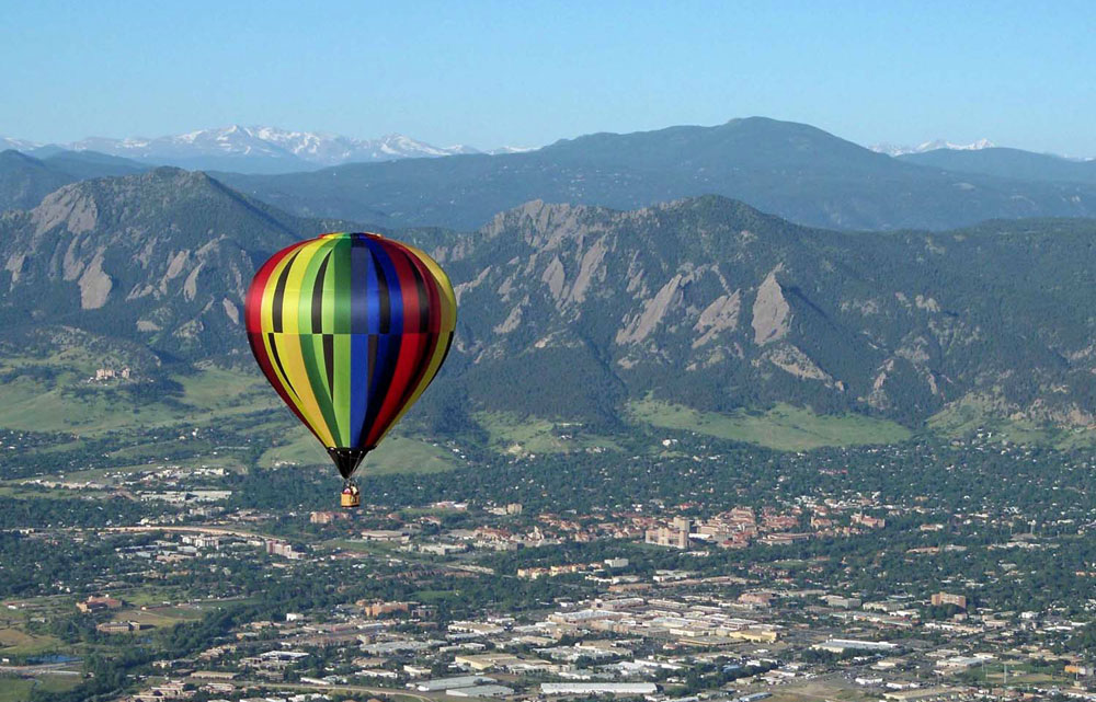A rainbow colored hot-air balloon floats over Boulder on a Colorado balloon ride
